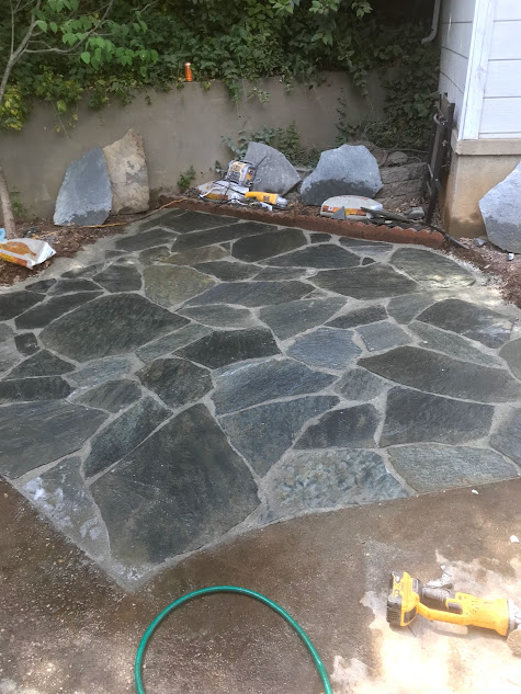 A hose is sitting on the ground next to a stone patio.