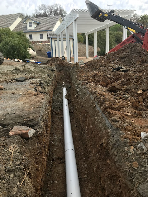 A white pipe is being installed in the dirt next to a house.