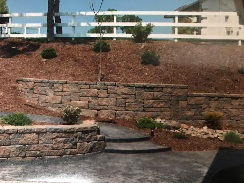 A stone wall with steps and a white fence in the background