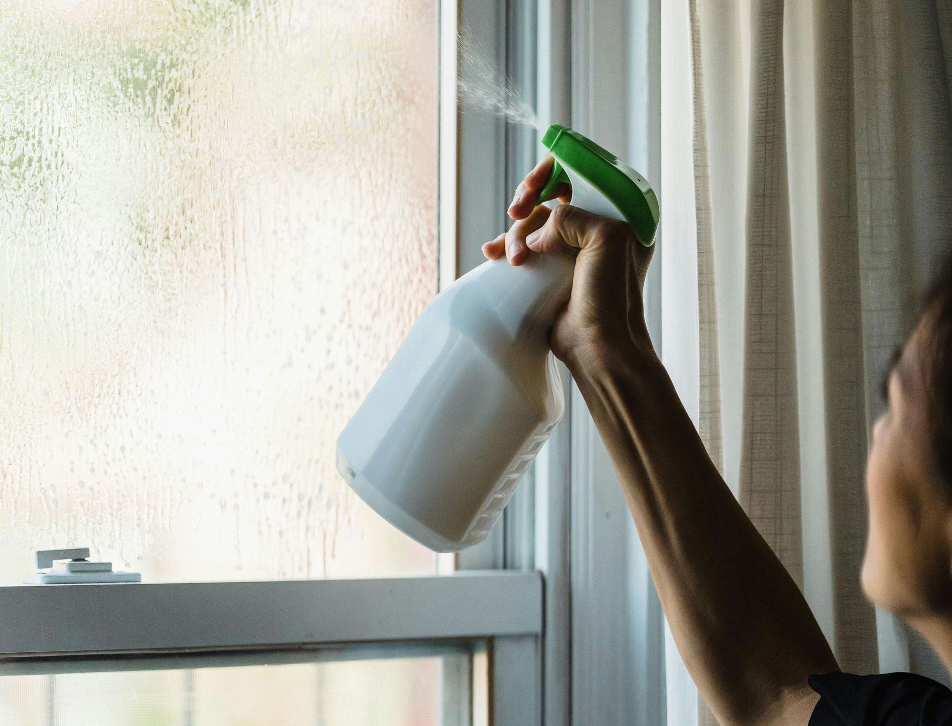 A person is spraying a window with a spray bottle.