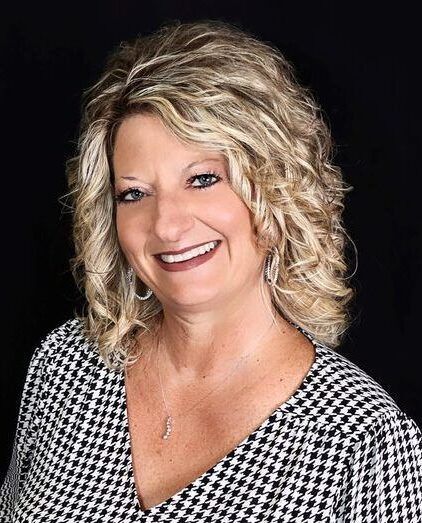 Agent Karen with blonde curly hair smiling, wearing a black and white patterned top.