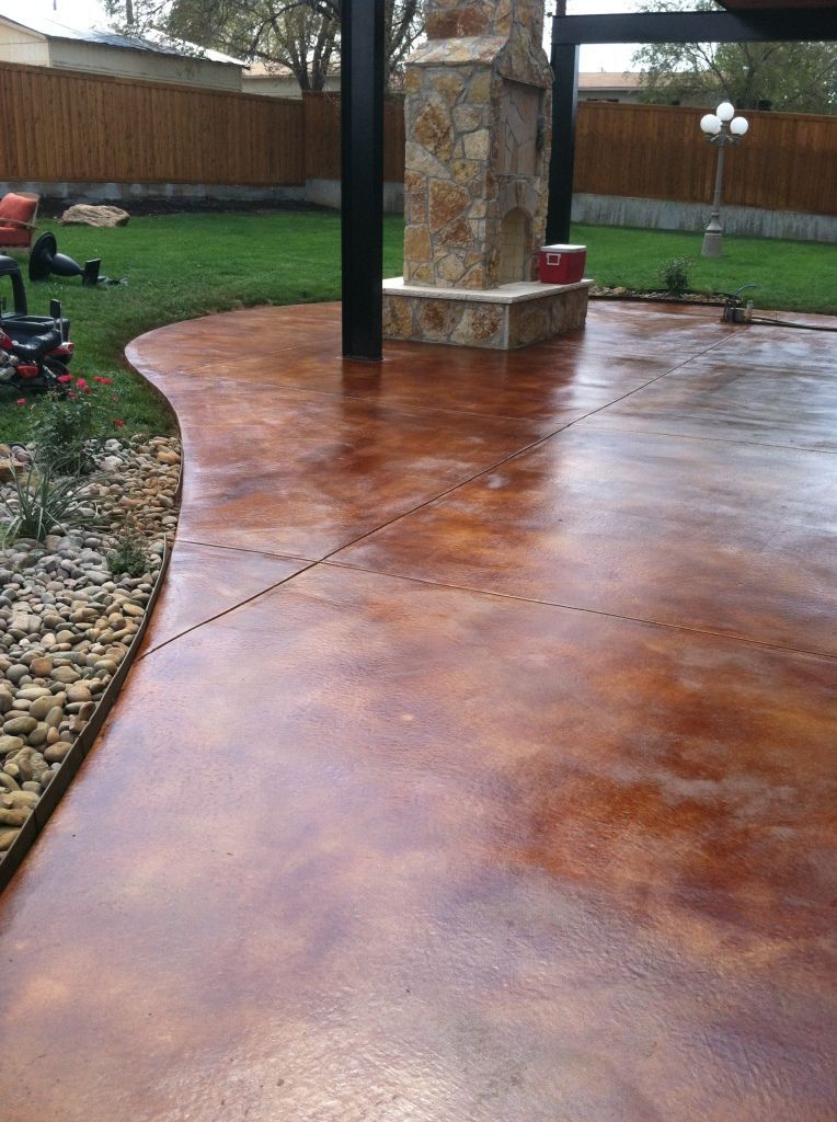 Brown stained concrete patio with an outdoor fireplace and green lawn.