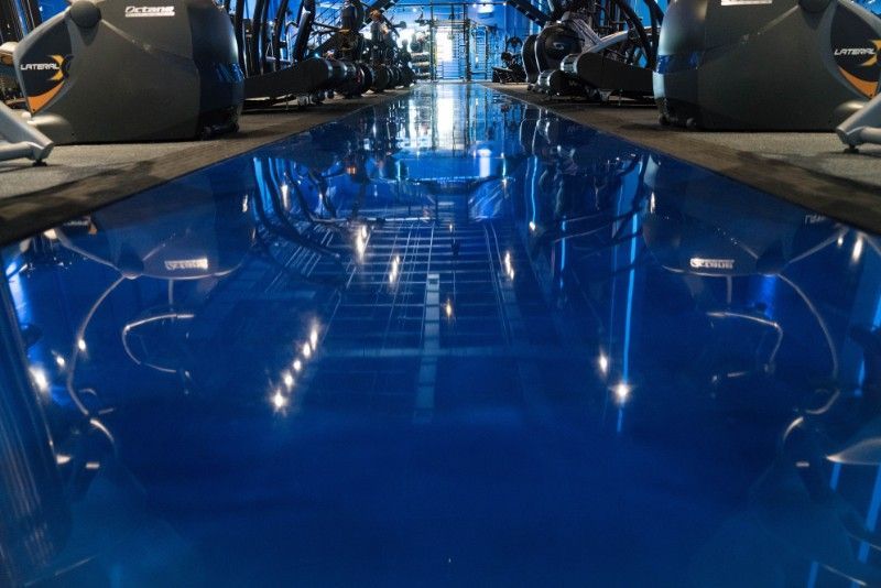 Blue reflective floor in a gym with exercise equipment lining the sides.