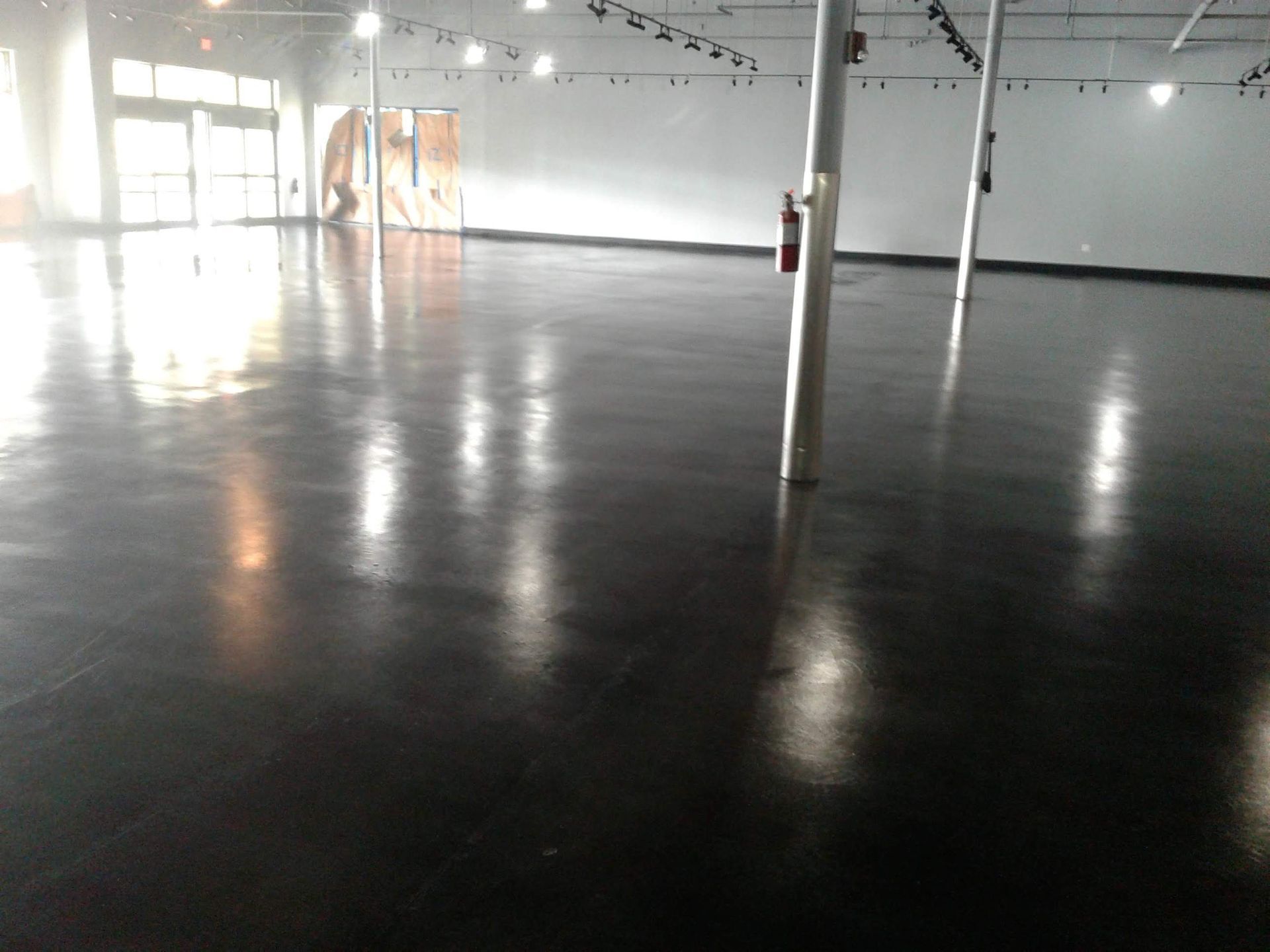 Glossy black floor in a large, empty, brightly lit room with support columns and closed doors.