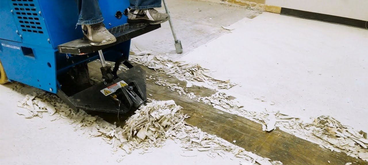 A person operating a blue floor scraper removing flooring in a room.
