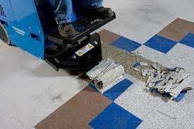 Floor scraper removing checkered tile. Blue machine, person standing, debris on the floor.