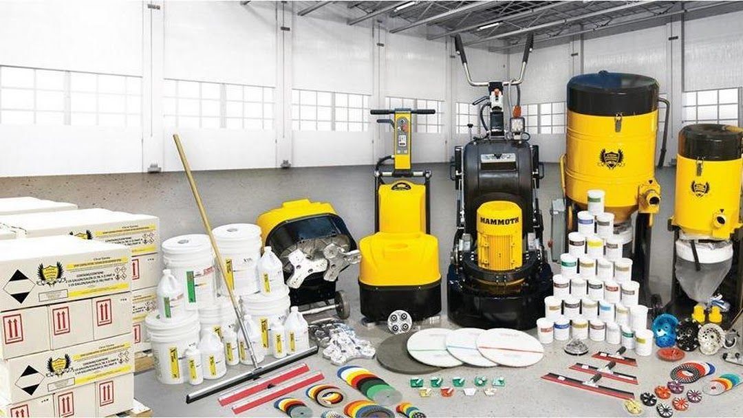 Warehouse scene with floor polishing equipment, chemicals, and supplies, predominantly yellow, black, and white.