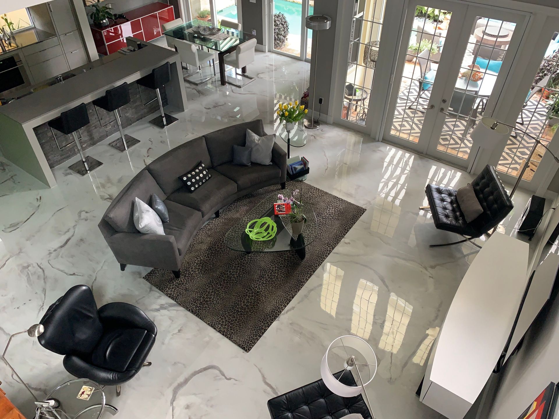 Modern living room with gray sofa, black chairs, marble floor, and doors to a patio.