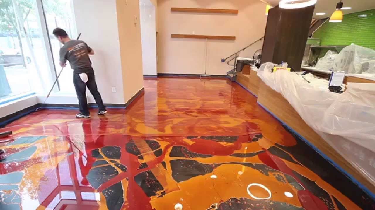 Man cleaning a store floor with orange, red, and black epoxy design. Shelves and a wrapped counter are in the background.