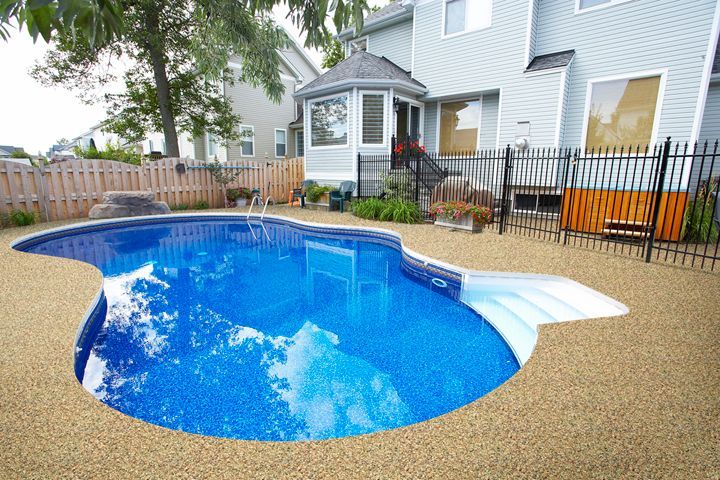 Backyard with a blue in-ground pool, tan concrete surround, and a multi-story house.