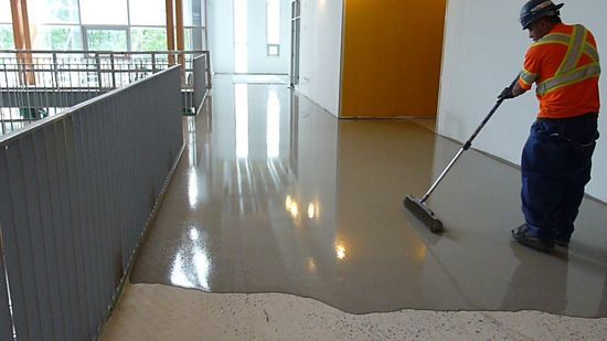 Construction worker smoothing wet floor coating in a building hallway.