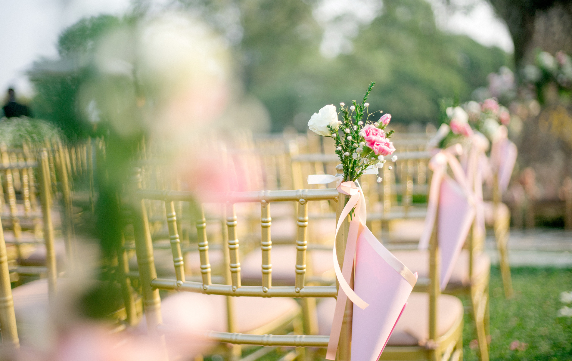 A row of chairs decorated with pink ribbons and flowers for a wedding ceremony.
