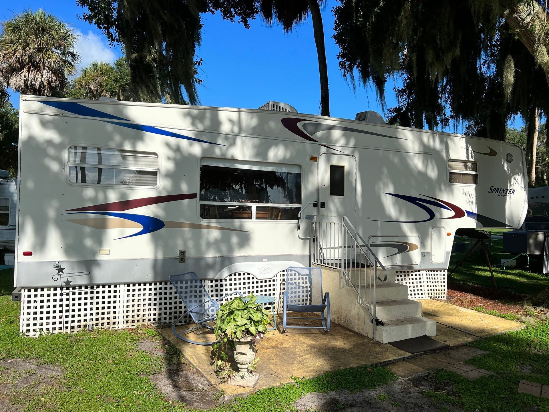 A white rv is parked in a grassy area with trees in the background.