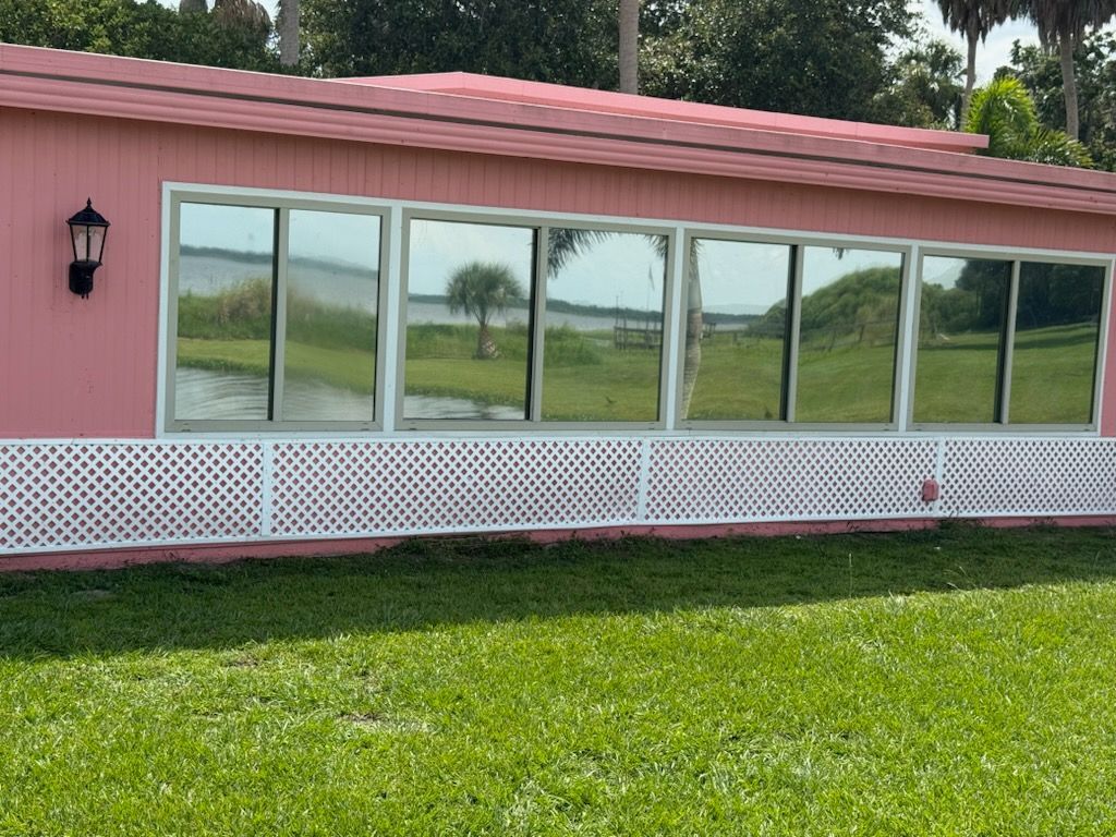 A pink house with a lot of windows is sitting on top of a lush green field.