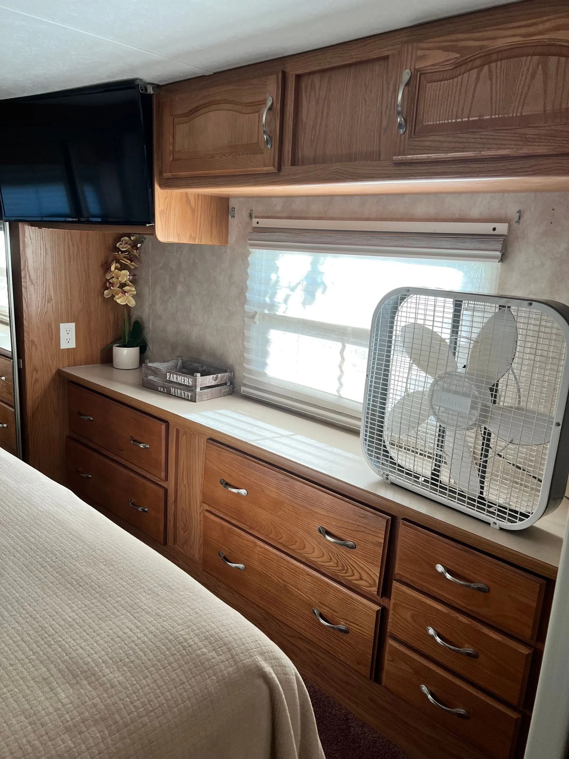 A bedroom in a rv with a fan on the counter.
