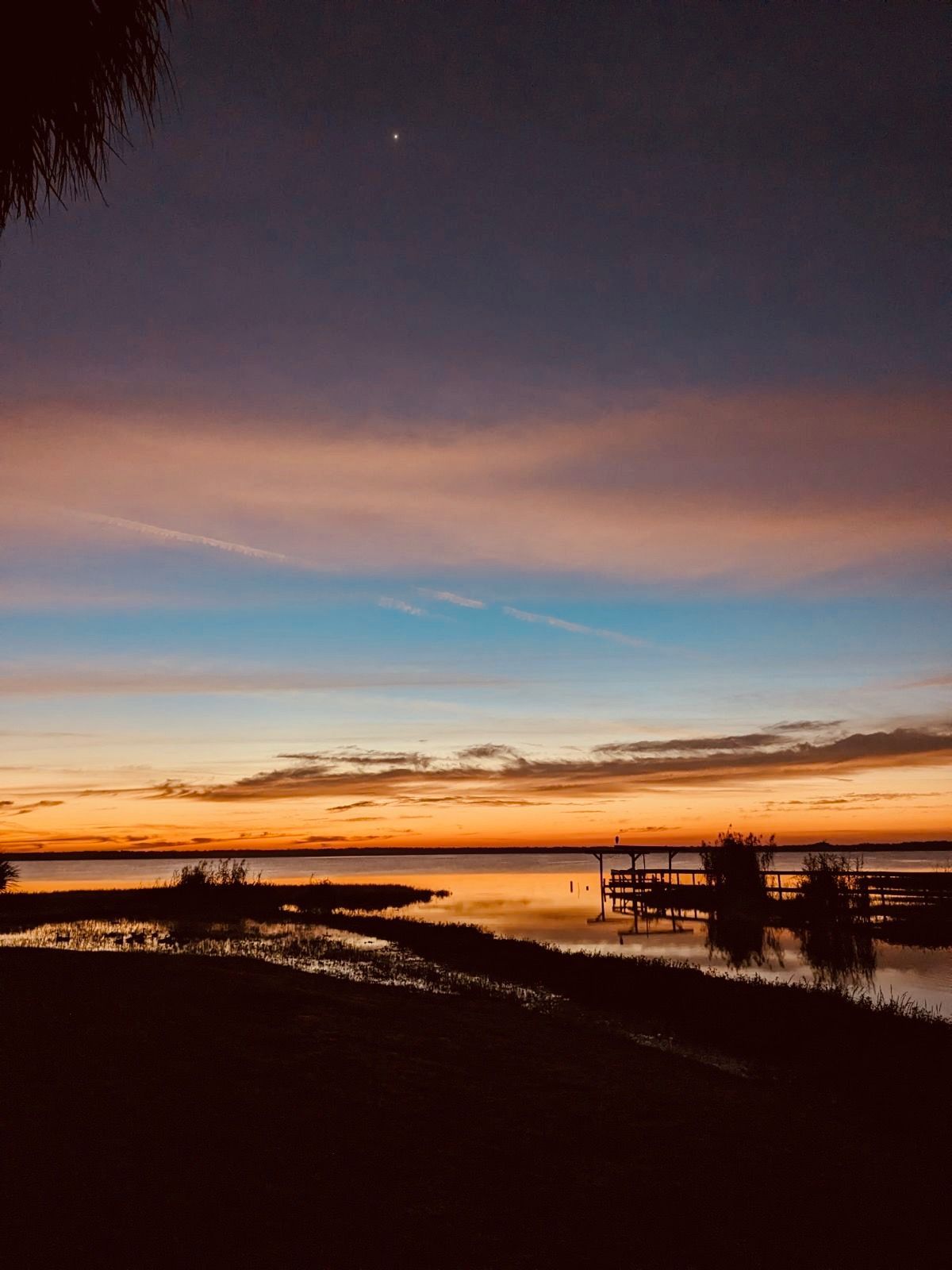 A sunset over a body of water with a dock in the foreground