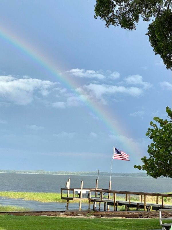 A rainbow over a body of water with an american flag in the foreground