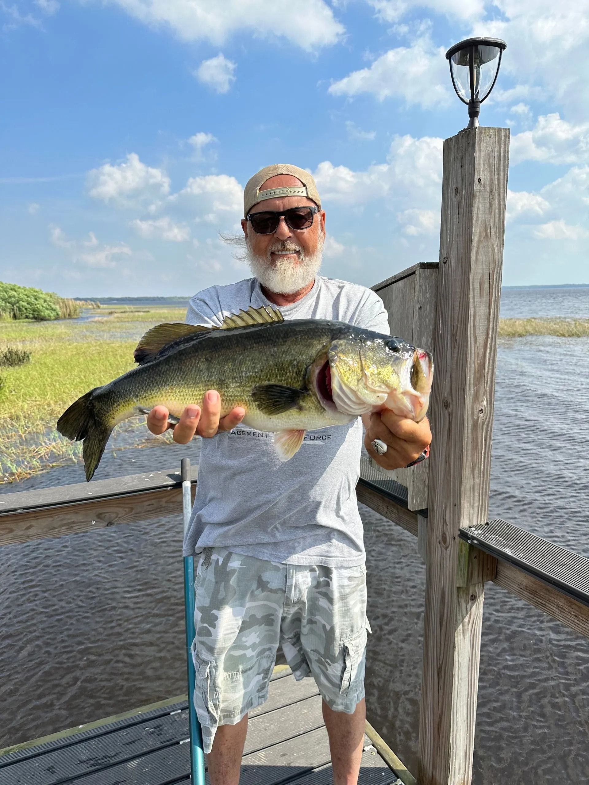 A man is holding a large bass on a dock.