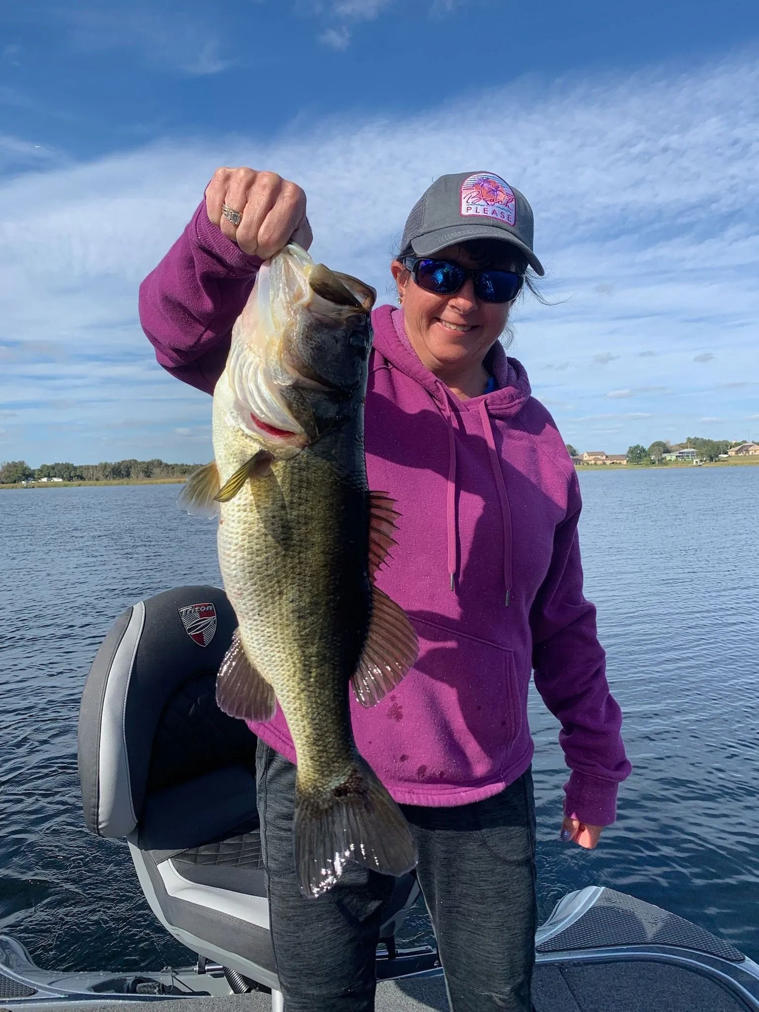 A woman is holding a large bass on a boat.