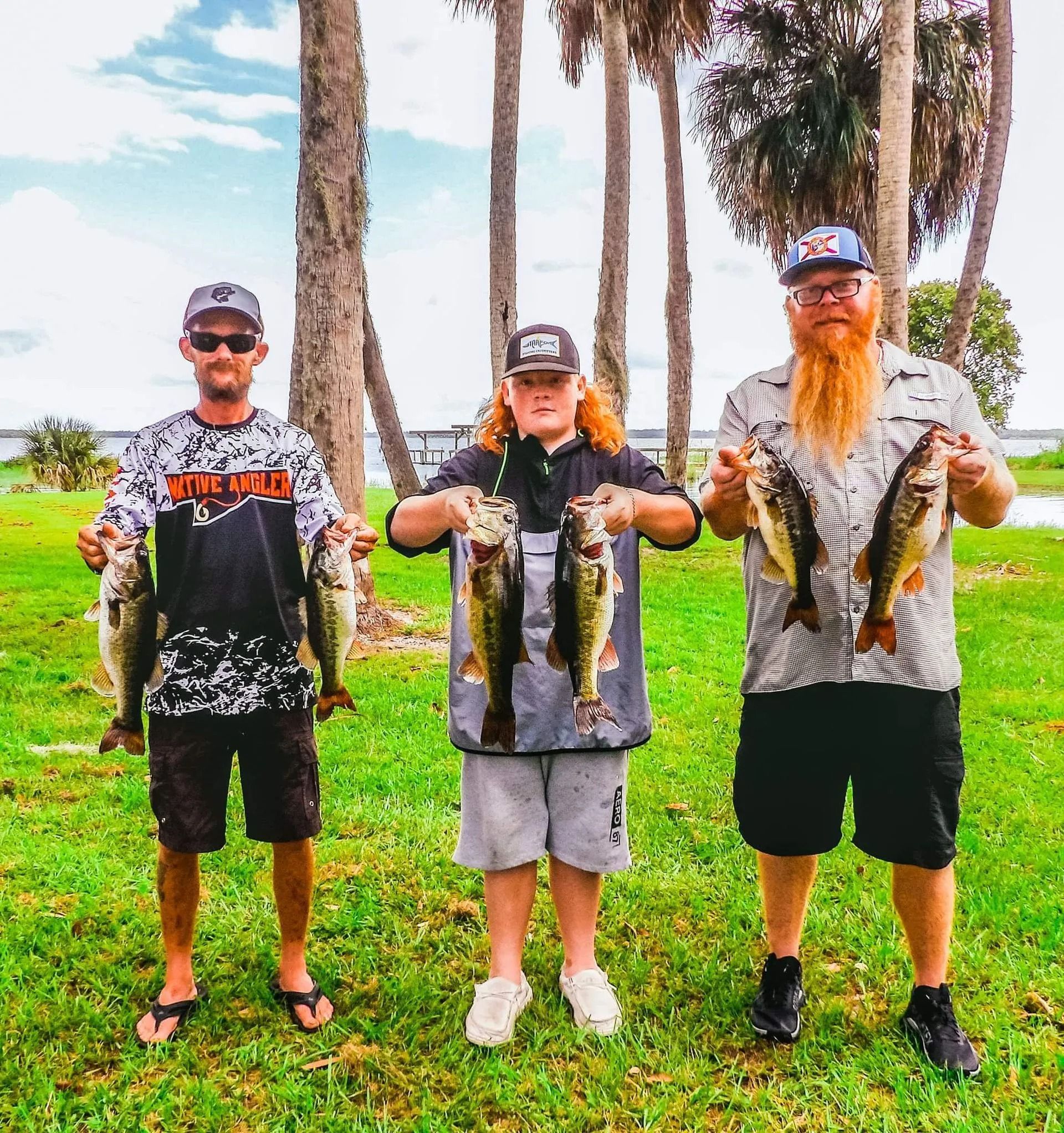 Three men are standing in a grassy field holding fish.
