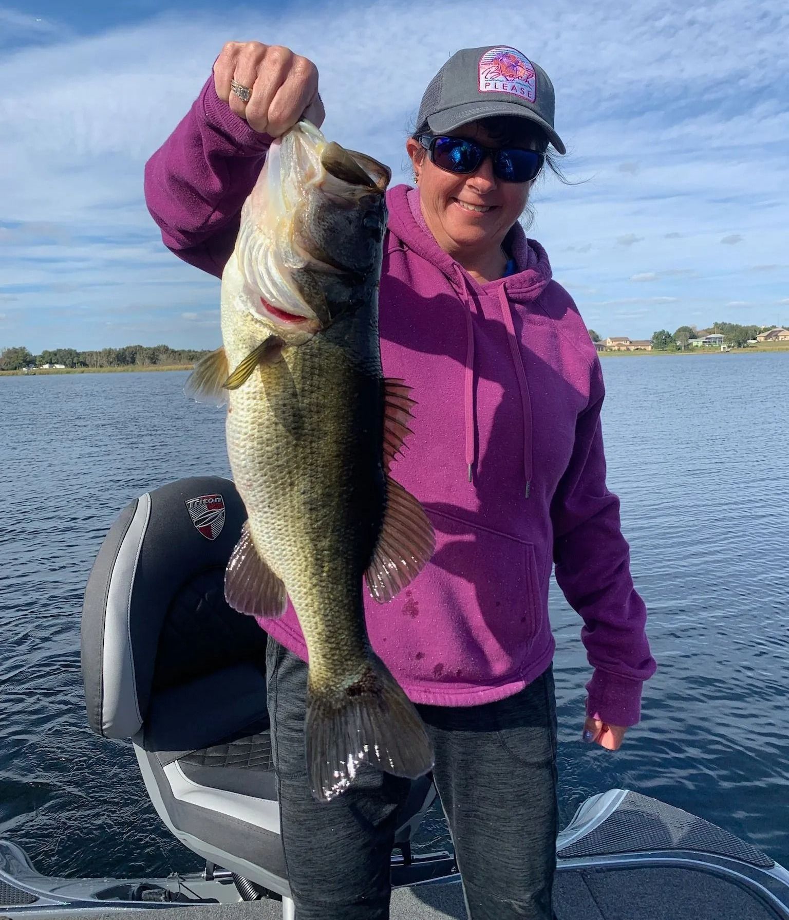 A woman is holding a large bass on a boat.