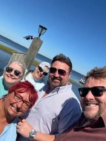 A group of people are posing for a picture in front of a body of water.