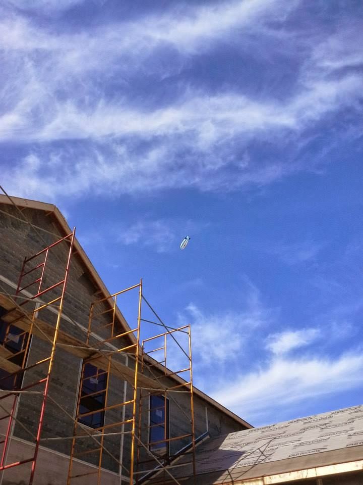 Building under construction with scaffolding against a blue sky with streaky clouds; a small object floats in the air.