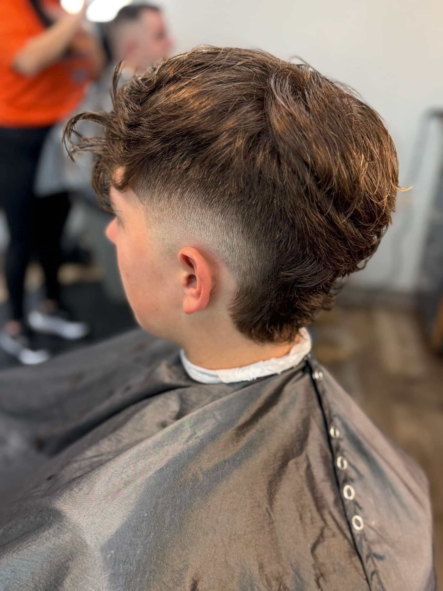 Side view of a short curly haircut with a faded cut in a barber chair, cape draped around the shoulders