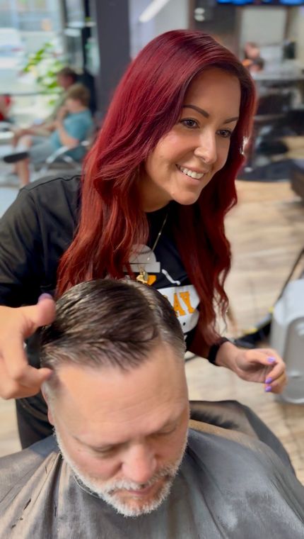 Woman giving a boy a haircut in a barbershop. She is smiling while cutting his hair.