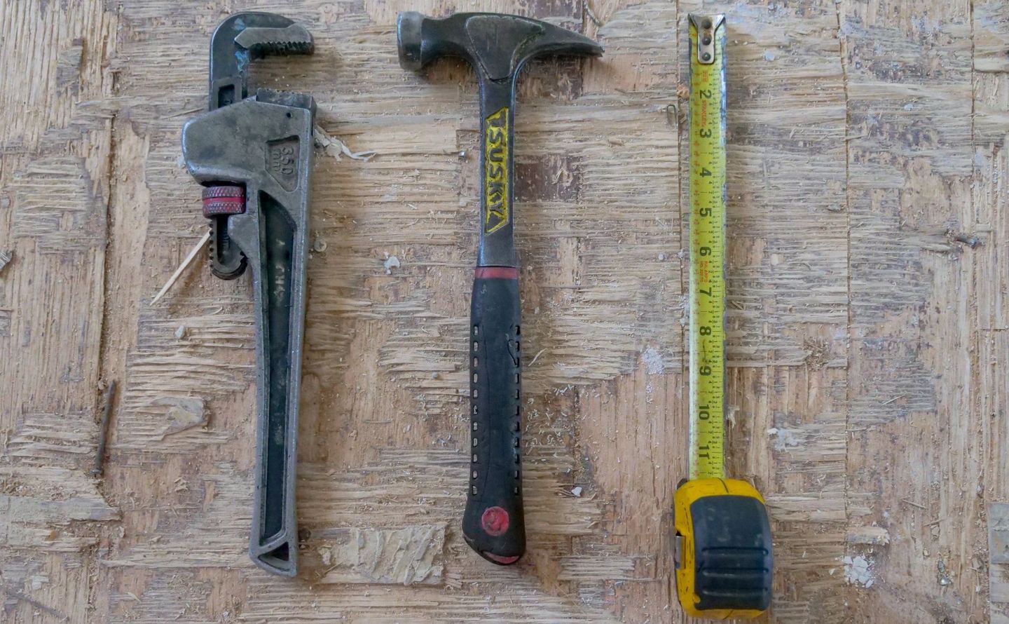 A hammer , wrench , and tape measure are on a wooden table.