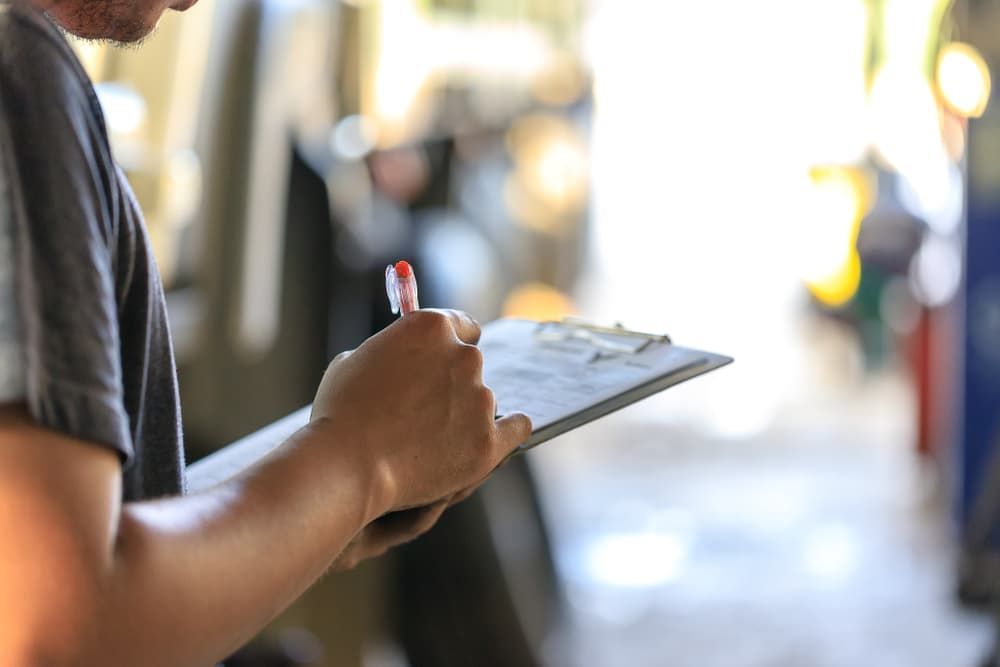 A Man Is Holding A Clipboard And Writing On It — Shamrock Mower & Motorcycle Repairs in Braemar, NSW