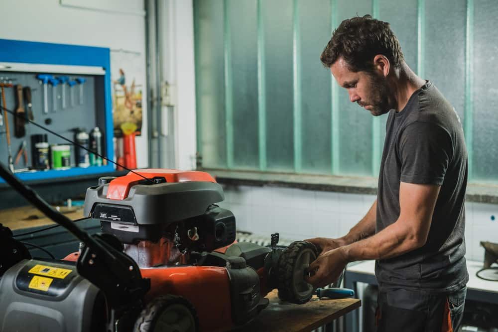 A Man Is Working On A Lawn Mower In A Garage  — Shamrock Mower & Motorcycle Repairs in Braemar, NSW