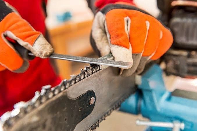 A Person Is Sharpening A Chainsaw With A Wrench — Shamrock Mower & Motorcycle Repairs in Braemar, NSW