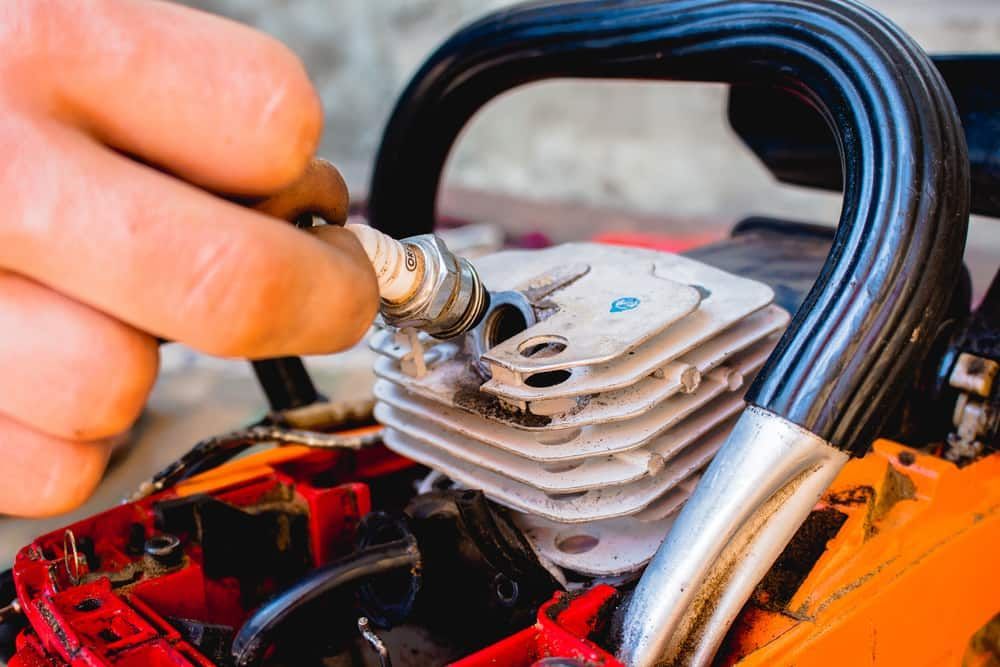 A Person Is Putting A Spark Plug Into A Chainsaw Engine  — Shamrock Mower & Motorcycle Repairs in Braemar, NSW