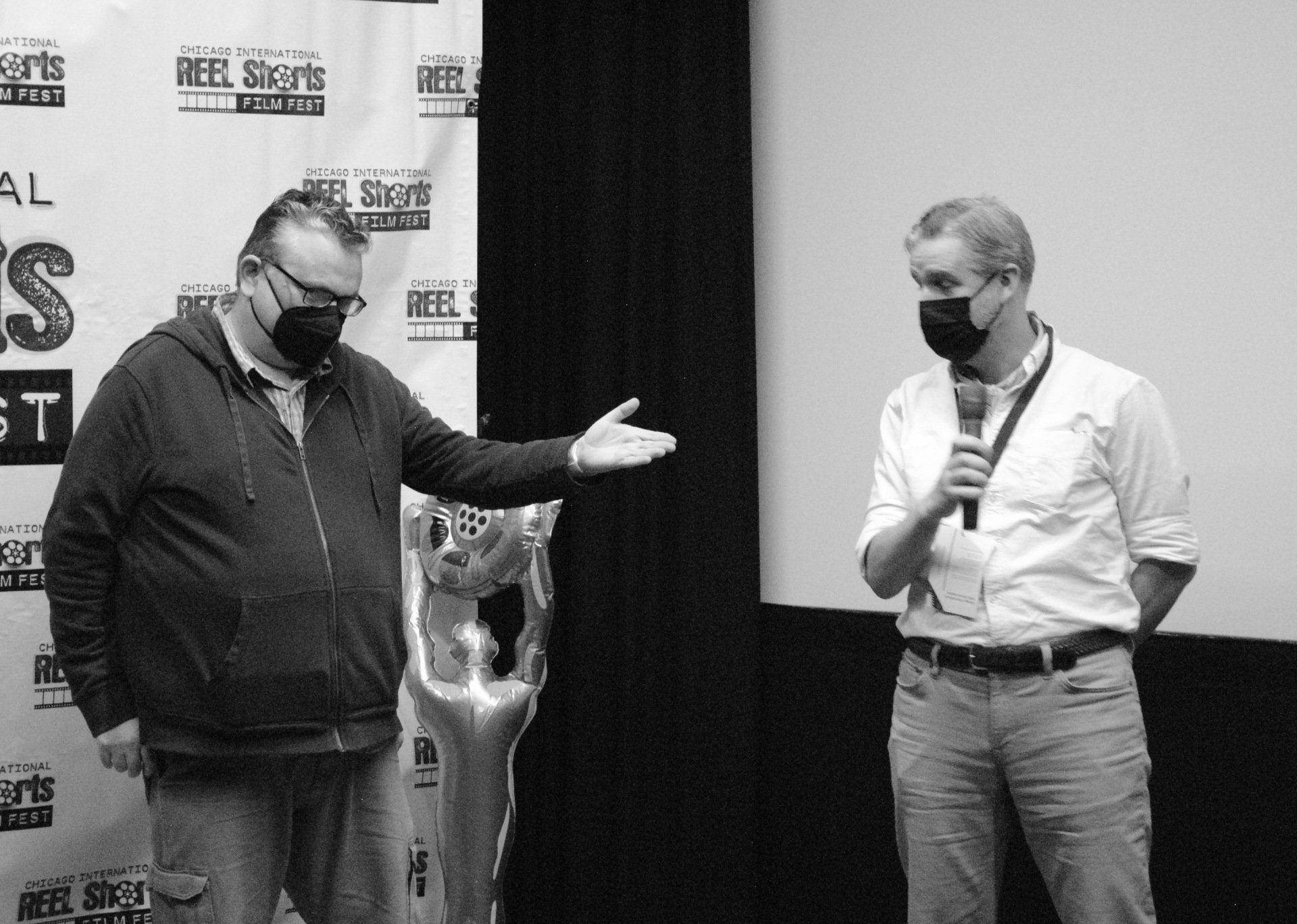 Two men wearing masks are standing next to each other in front of a sign that says reel secrets