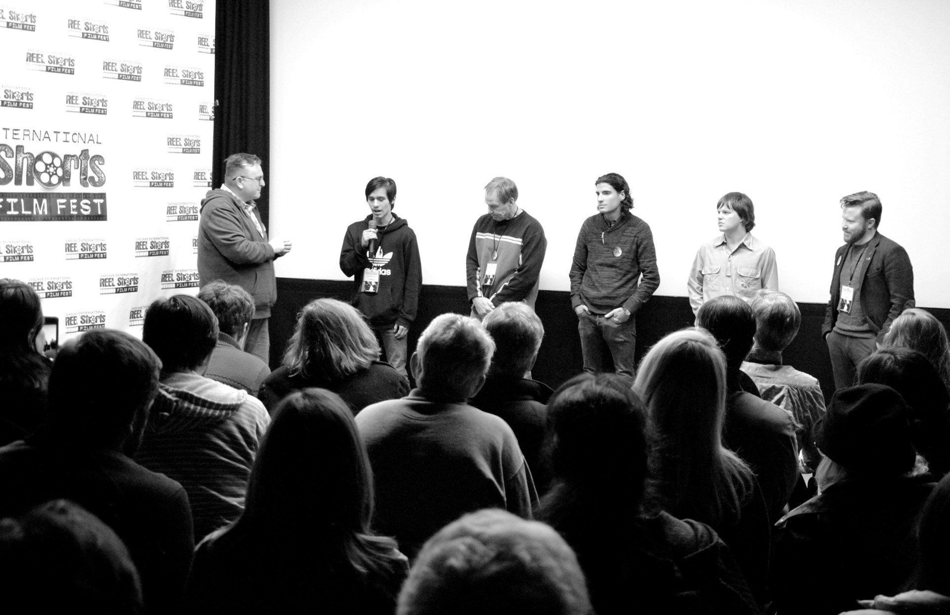 Panel of men on stage, speaking to an audience at a film festival. Black and white.