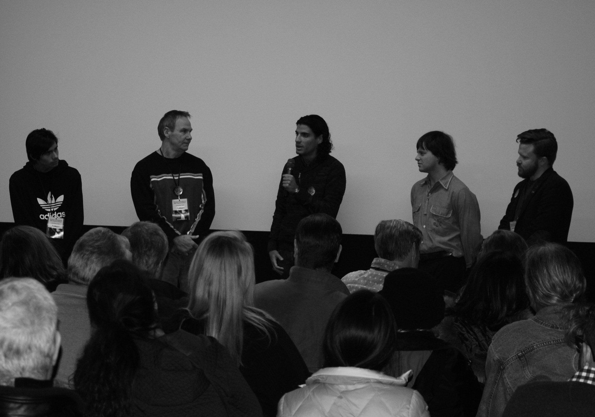 Panel of five men on stage, speaking to an audience. Black and white photo.