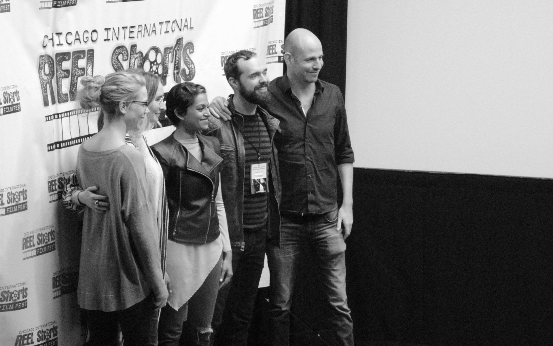 Group of five people posing, smiling, in front of a Chicago film festival backdrop. Black and white.