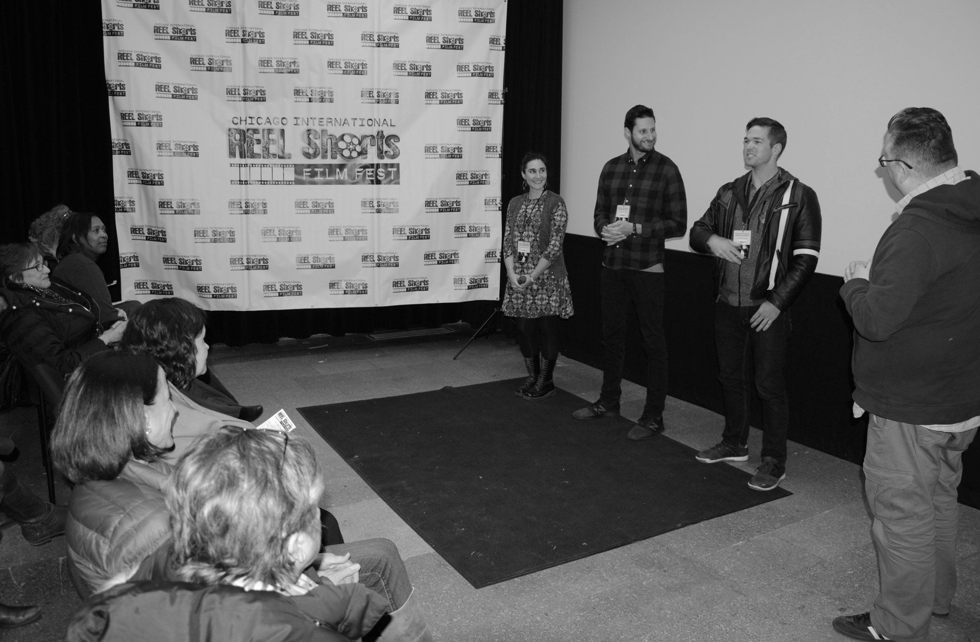 Panelists on stage at film festival, addressing seated audience; black and white.