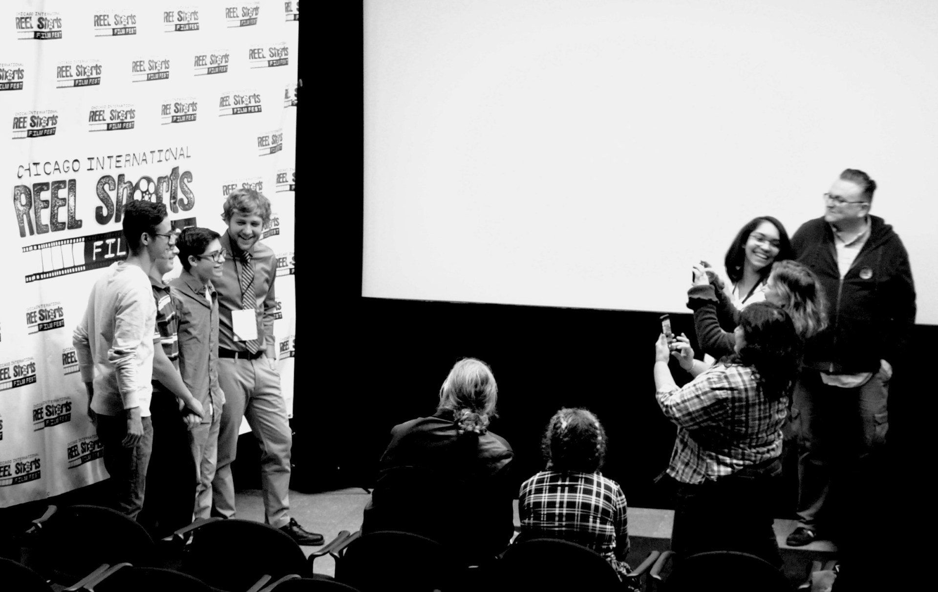 A group of people are standing in front of a screen taking a selfie.