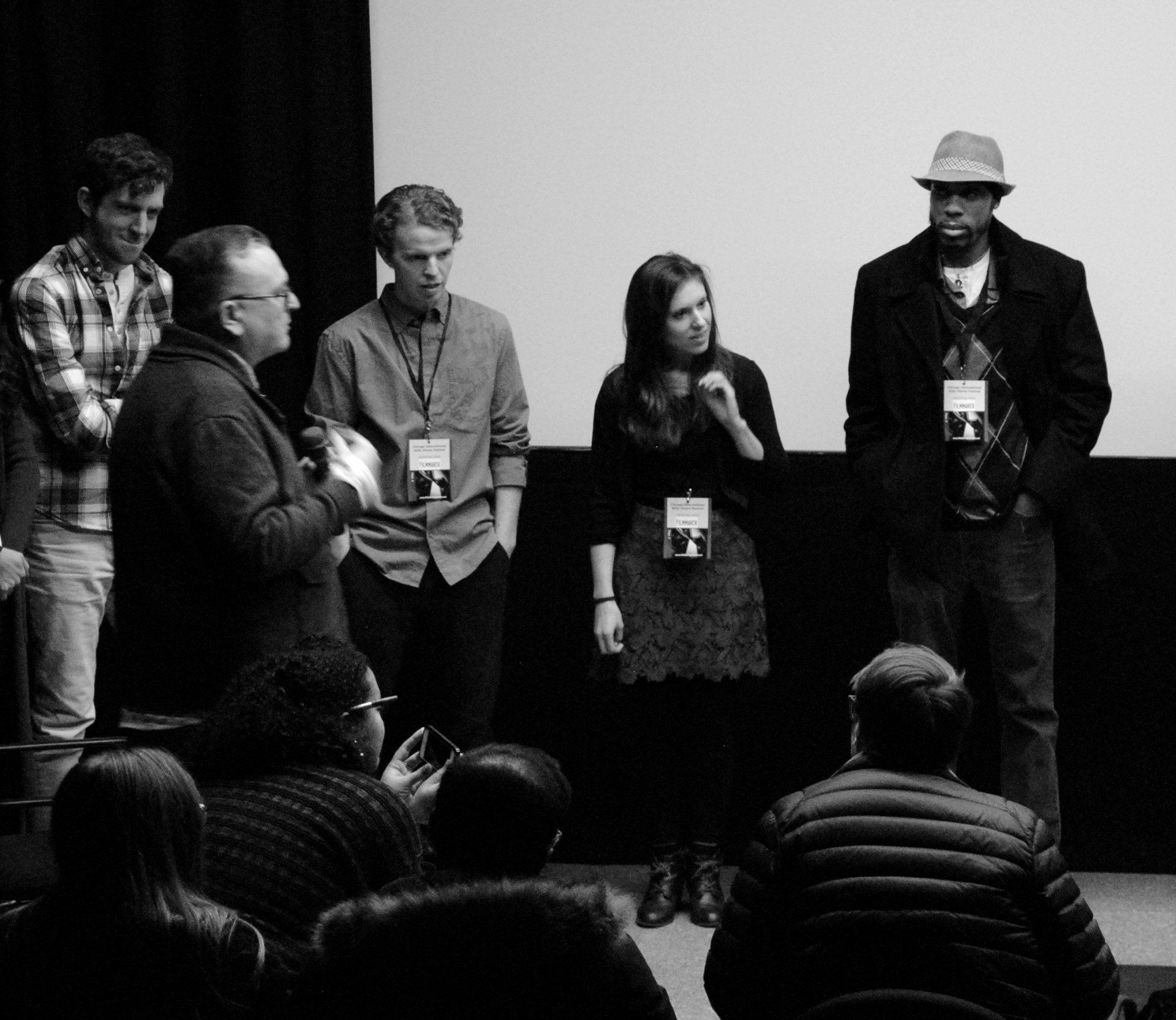 Panel of five people speaking in front of a seated audience. Black and white photo.