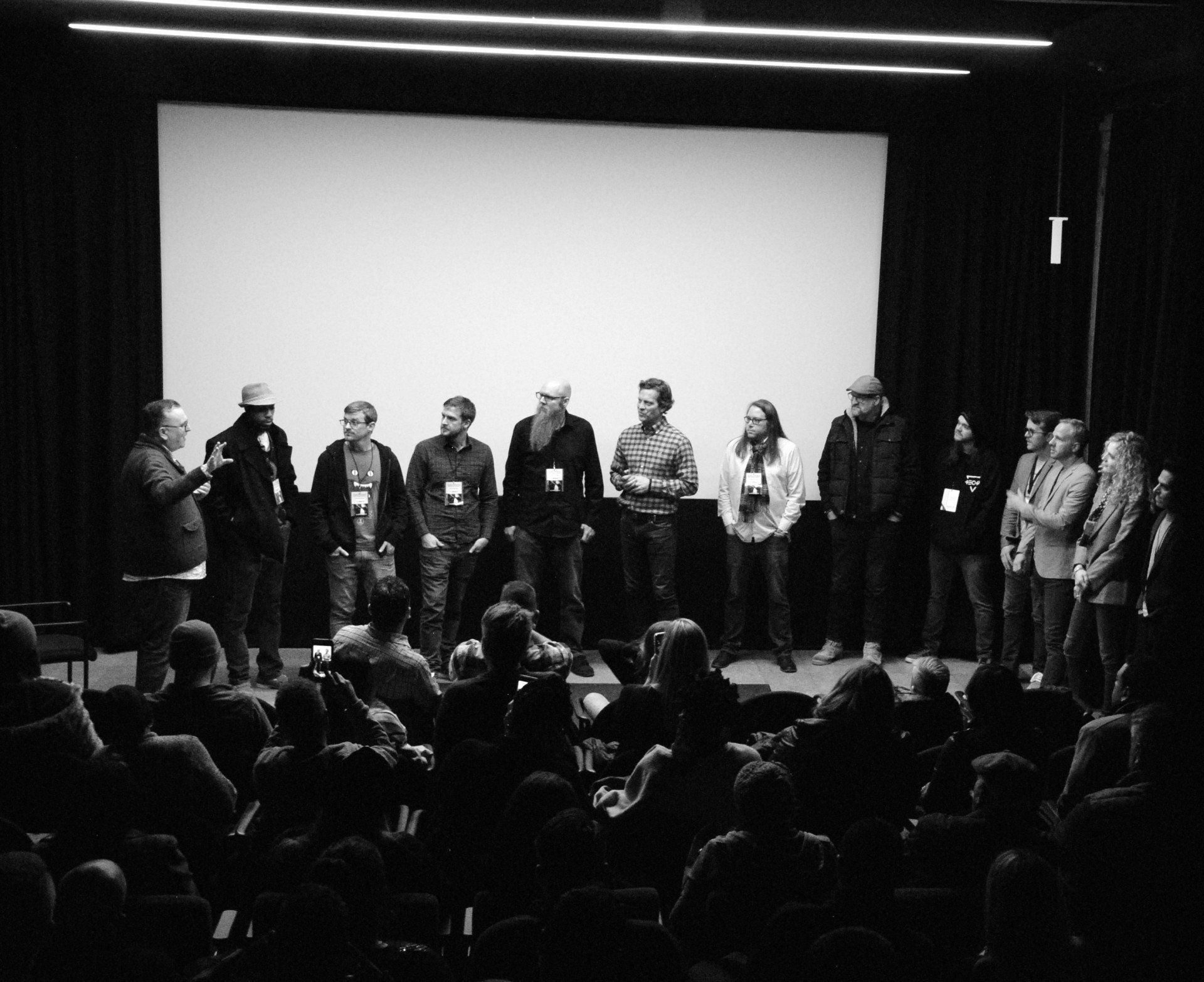 A group of people on stage in a theater, facing an audience. They're likely being introduced at a film screening.