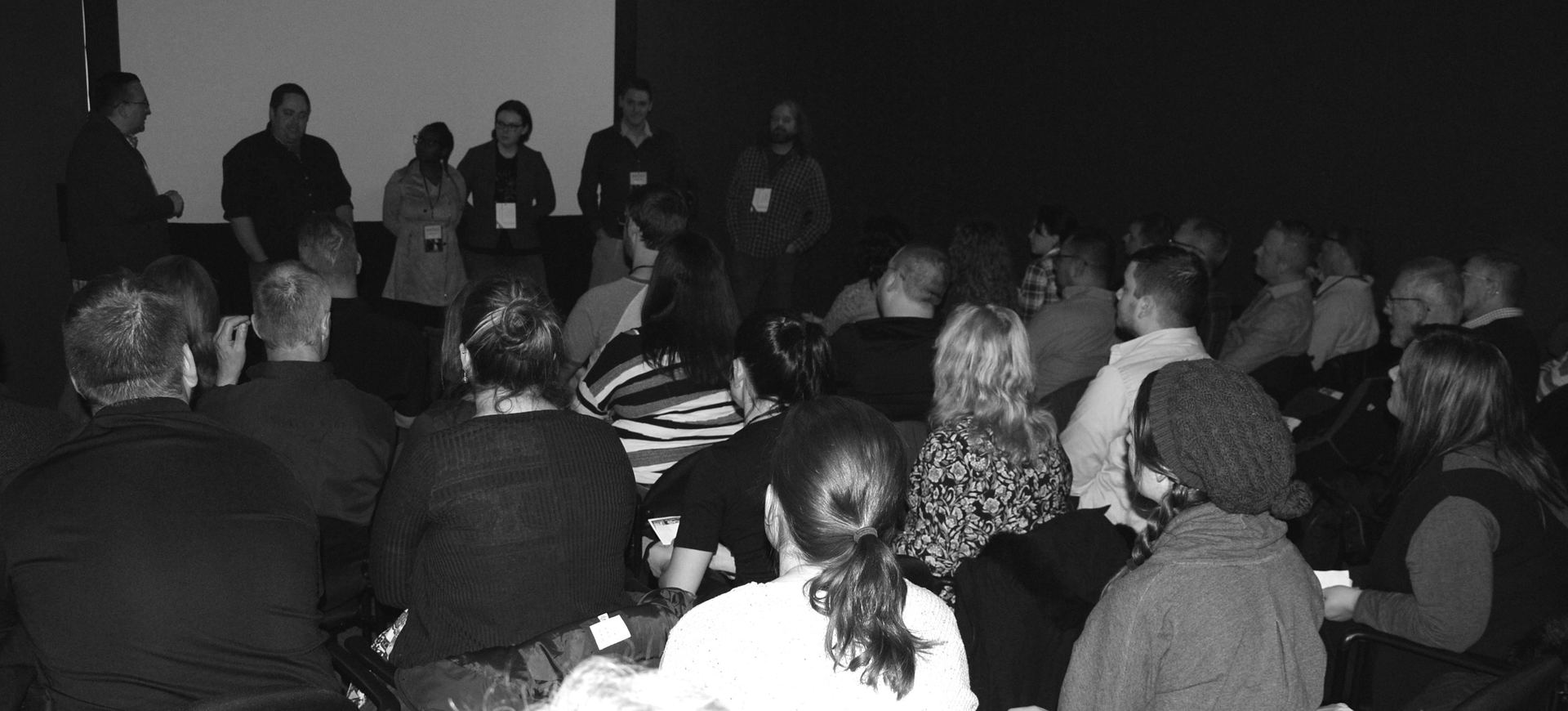 A panel of people stands on a stage in front of an audience at a conference.