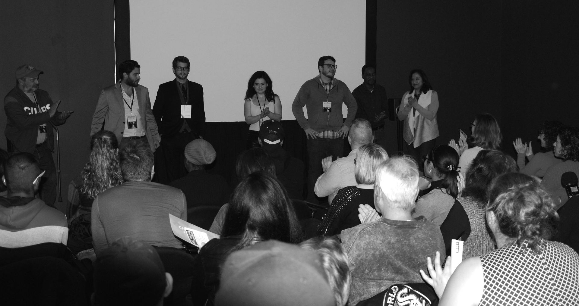 Panel discussion onstage, group of speakers facing audience in a dimly lit auditorium.
