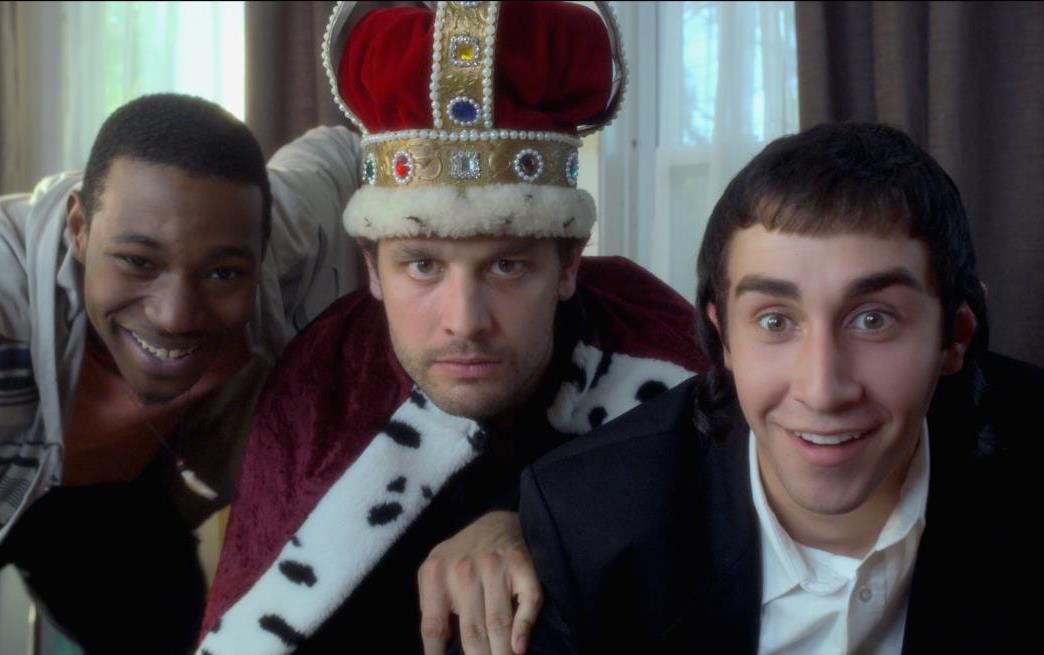 Three men are posing for a picture with one wearing a crown