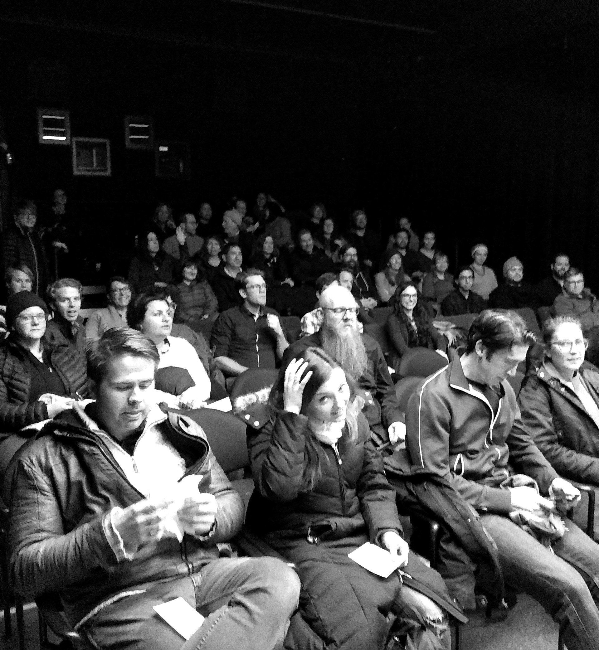 Audience in a dark theater. People seated, watching a performance or presentation.