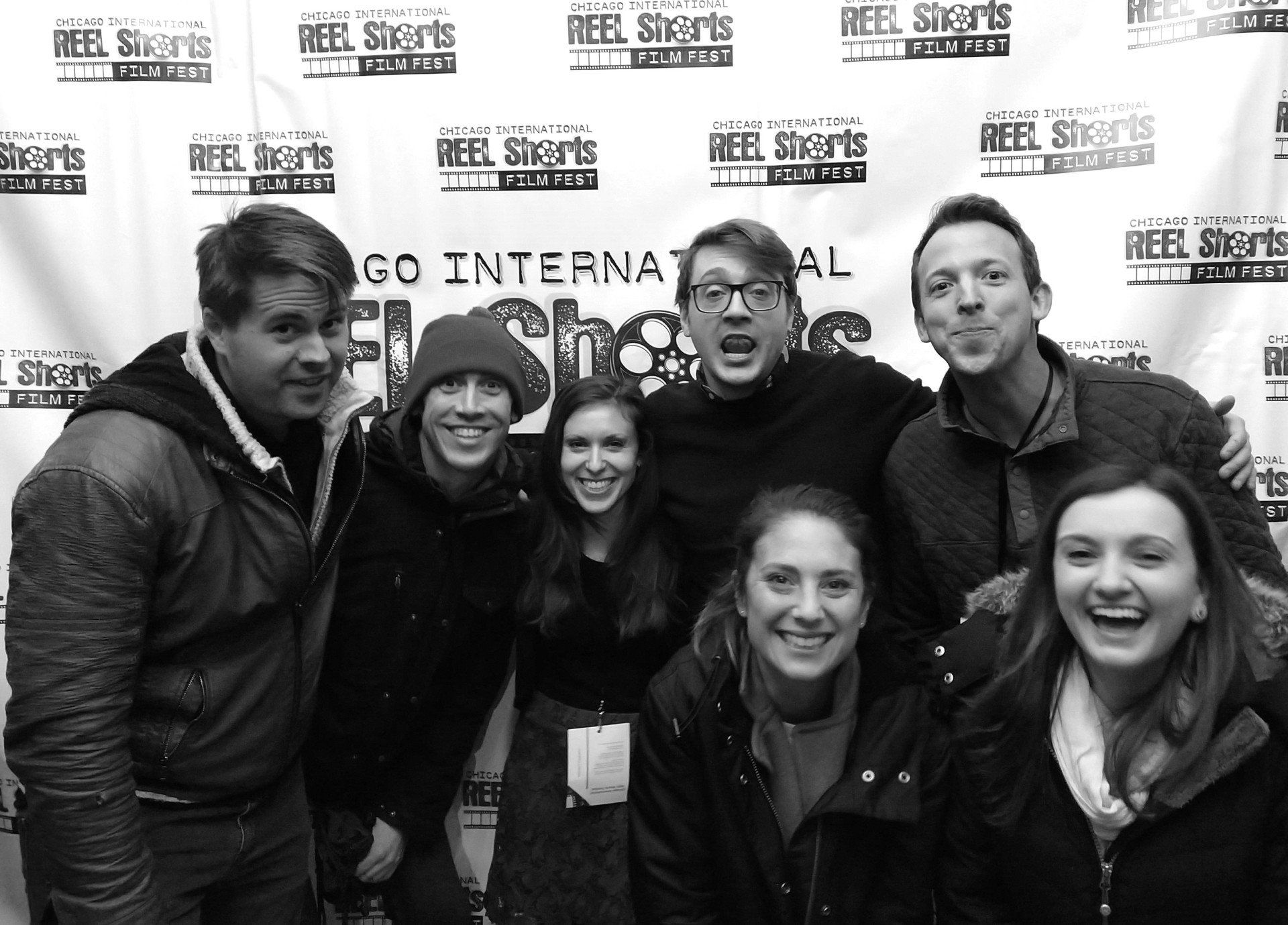 Group photo at the Chicago International Reel Shorts. Seven smiling people pose in front of a backdrop. Black and white.
