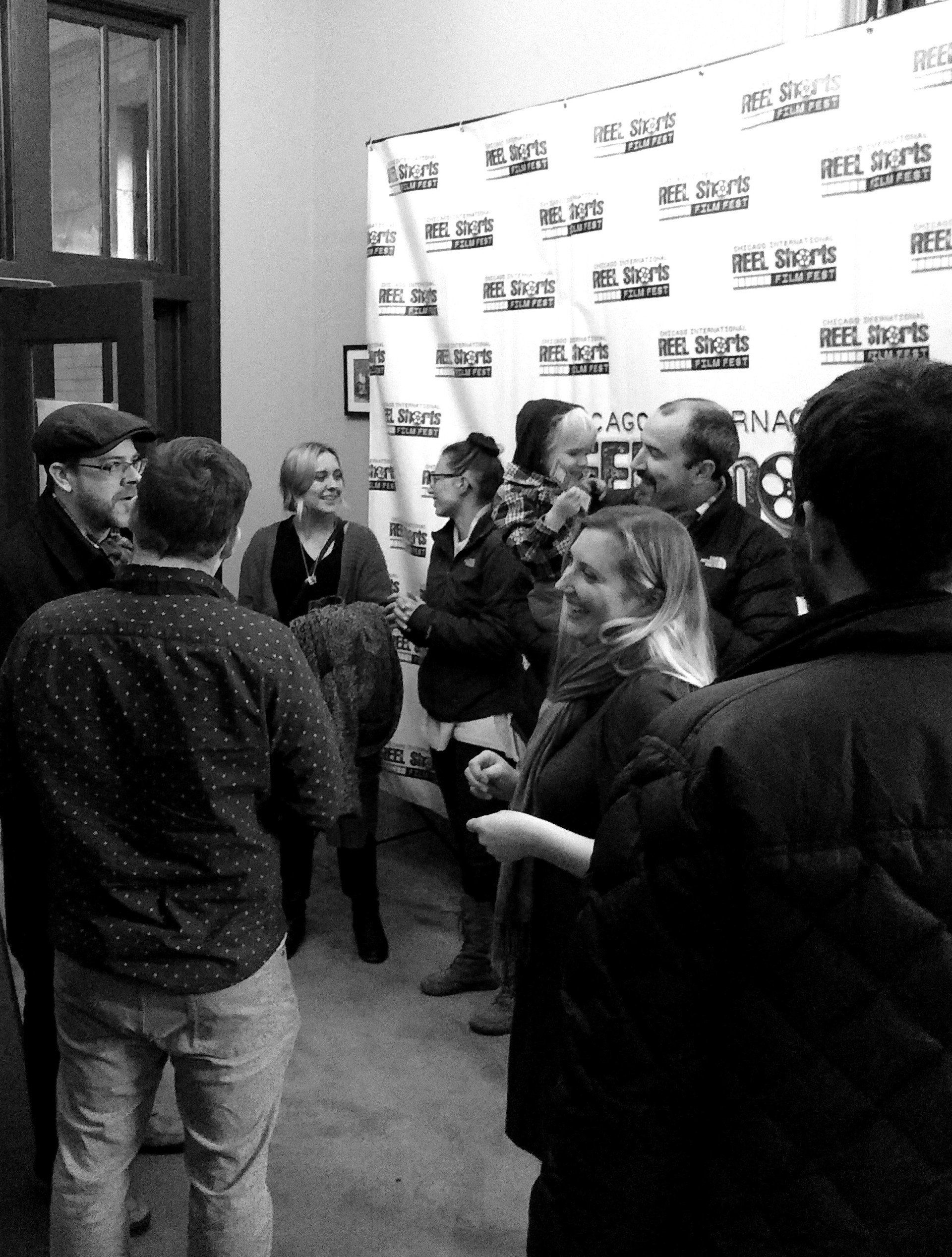 People in a room talking near a backdrop, black and white.