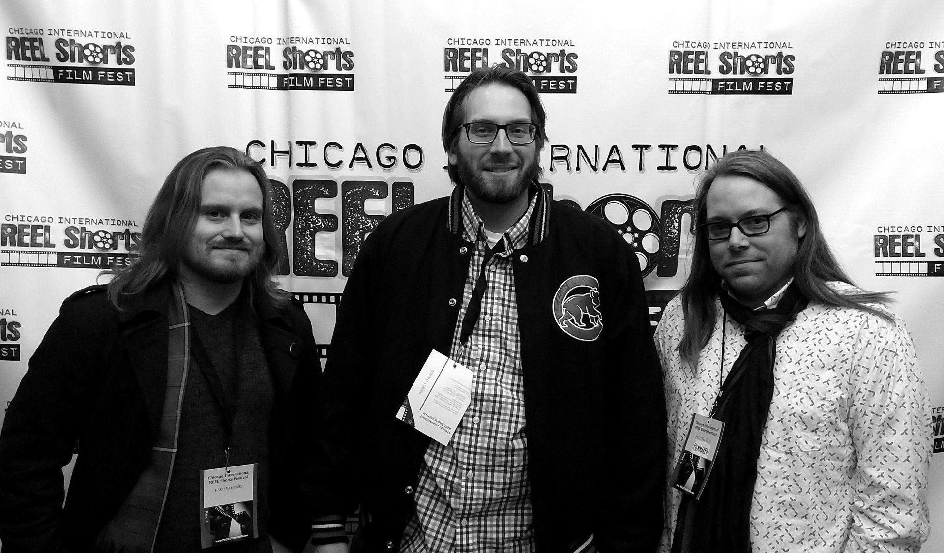 Three men at a Chicago International REEL Shorts event. One wears a jacket, all have lanyards, posing for a photo.