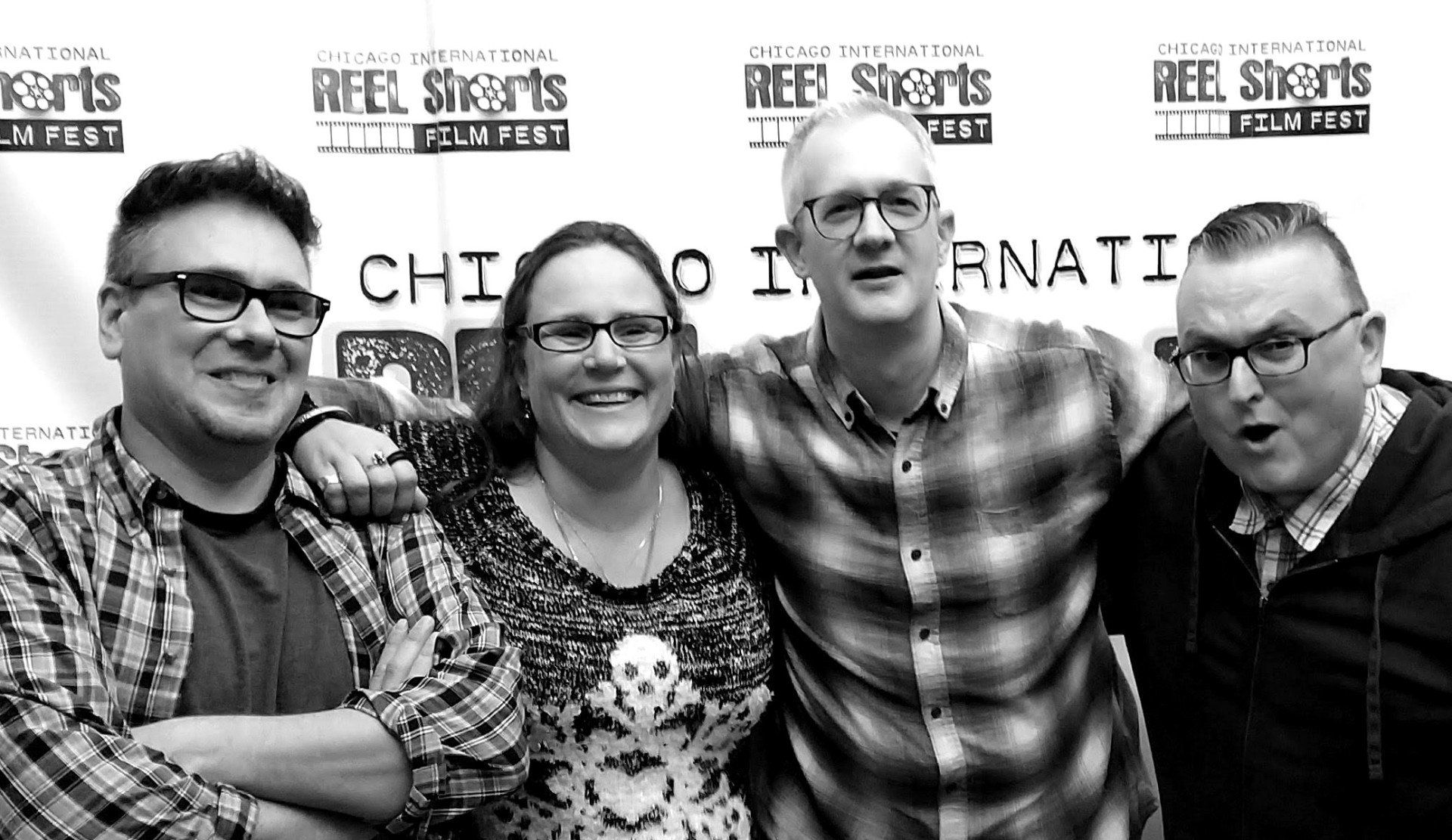 Four people smiling, posed in front of a film festival backdrop, wearing glasses, varying expressions.